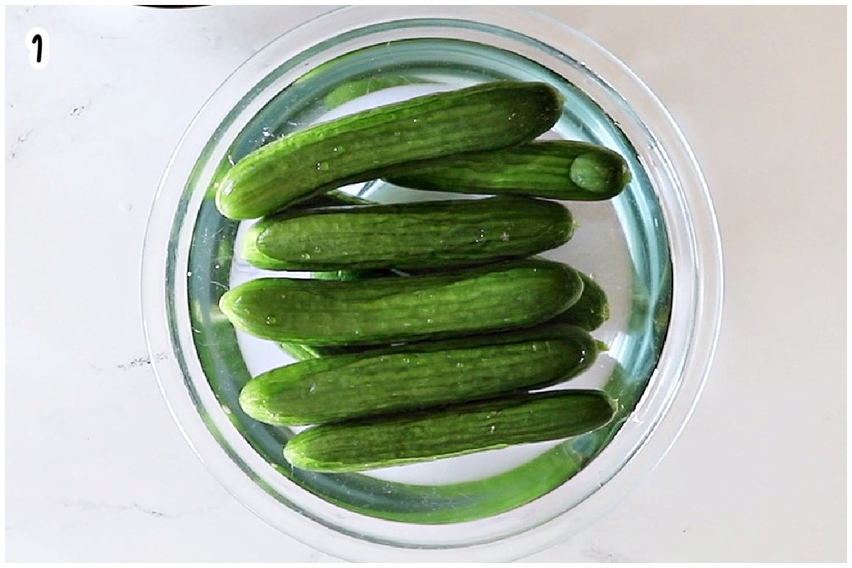 Persian cucumbers soaking in water in a glass bowl.