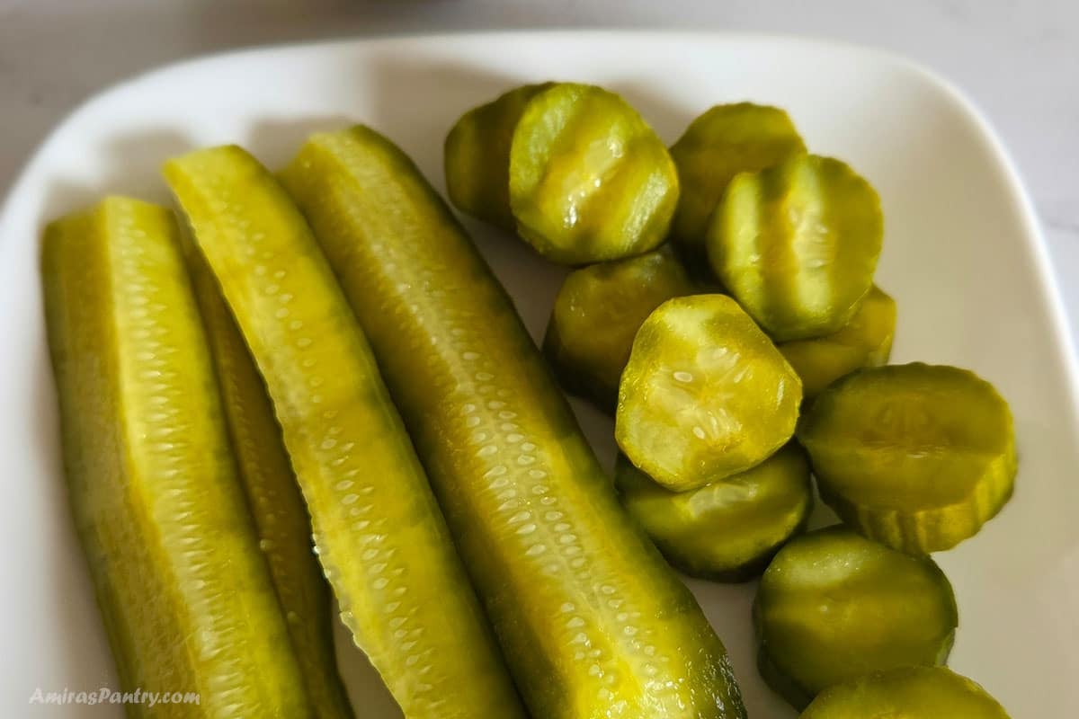 Close-up of pickled cucumber spears and round slices on a white plate.