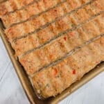 Angled overhead view of sheet pan kebab strips scored into individual portions on a gold baking pan.