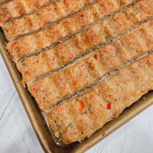 Angled overhead view of sheet pan kebab strips scored into individual portions on a gold baking pan.