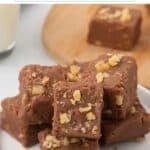 Pinterest pin titled 'Fantasy Fudge with Jet-Puffed' showing stacked squares of chocolate fudge topped with chopped nuts on a white plate, with more fudge on a wooden board and a glass of milk in the background.