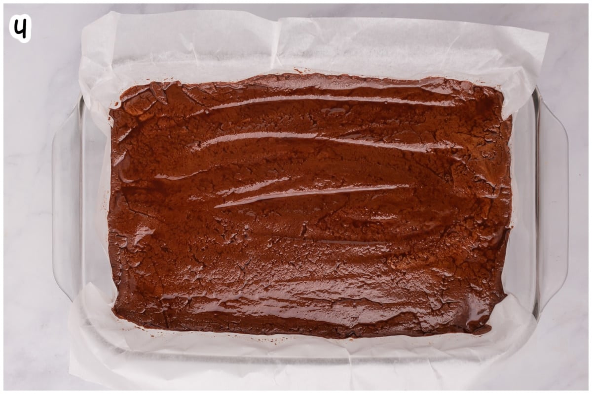 Overhead view of smooth chocolate fantasy fudge spread evenly into a parchment-lined glass baking dish, ready to set.