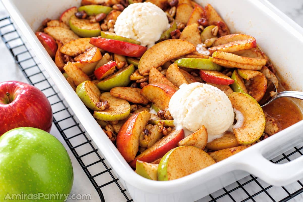 A white oven dish with baked apple slices and topped with vanilla ice cream.