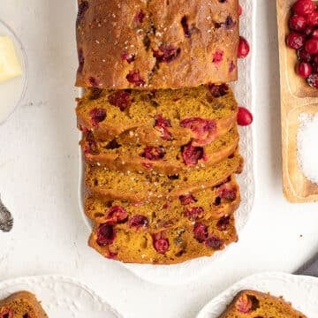 Close up overhead shot of sliced pumpkin cranberry bread on a platter, surrounded by cranberries and butter.