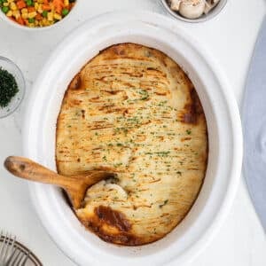 Slow cooker cottage pie with a golden, fork-ridged potato topping and a wooden spoon taking out a serving.