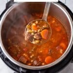 Ladle of beef barley soup with beef, barley, and carrots, held above an Instant Pot.
