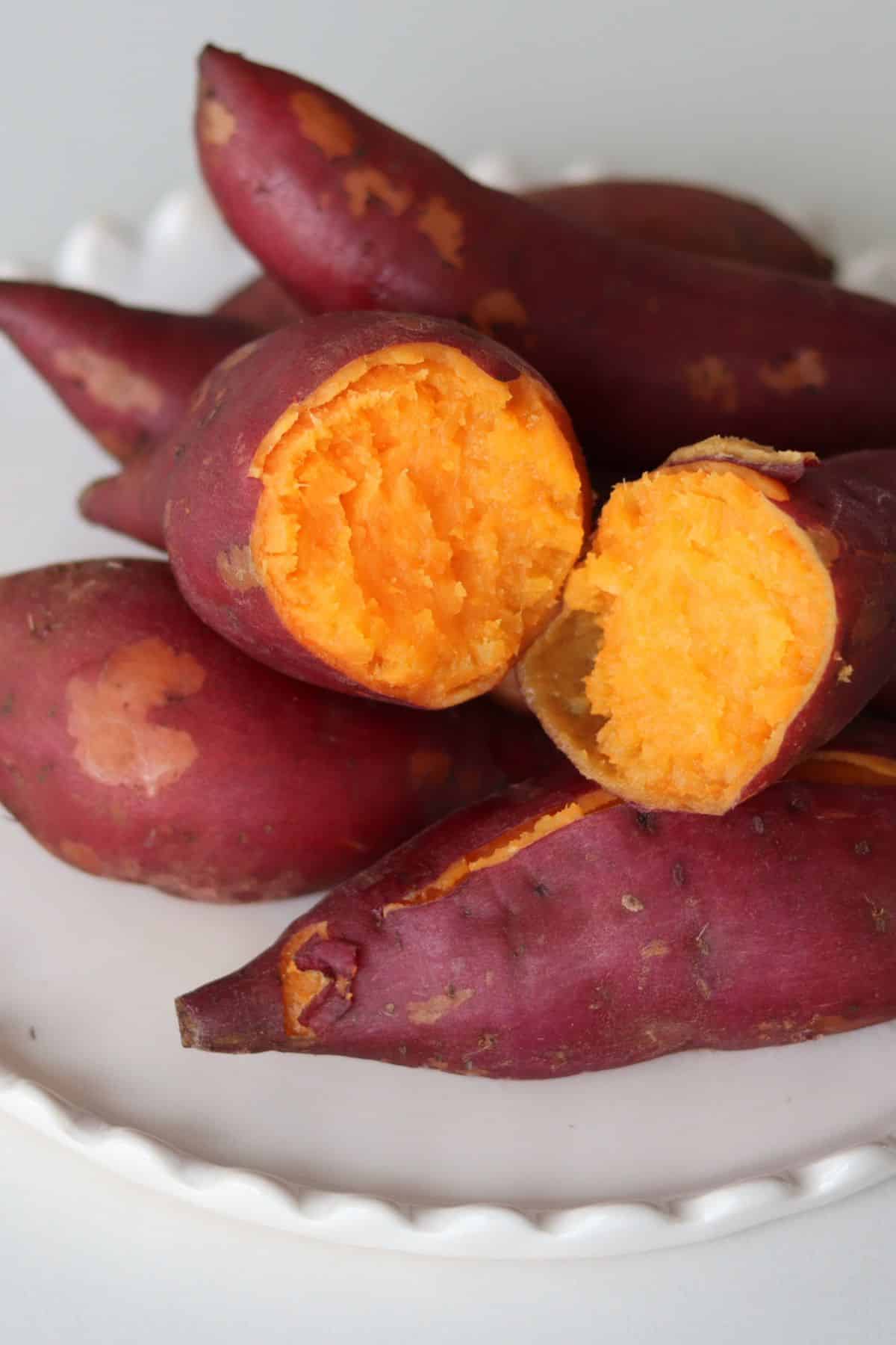 Microwaved sweet potatoes on a white plate, one split open to show orange flesh.