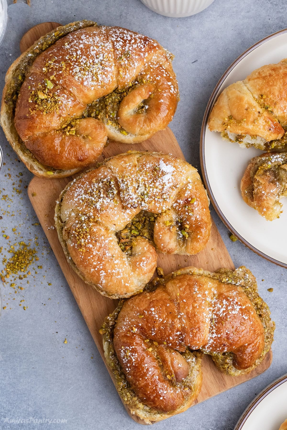 Three pistachio-filled croissants dusted with powdered sugar and crushed pistachios on a wooden board.