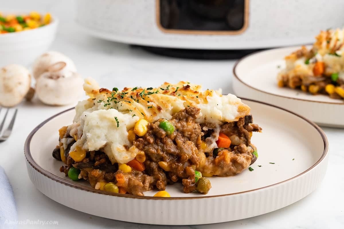 A slice of slow cooker cottage pie on a plate, with beef and vegetable filling under a golden mashed potato topping.